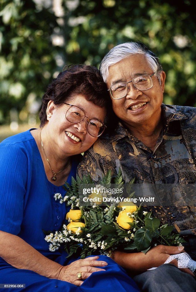 Mature couple holding bouquet of flowers, smiling, portrait