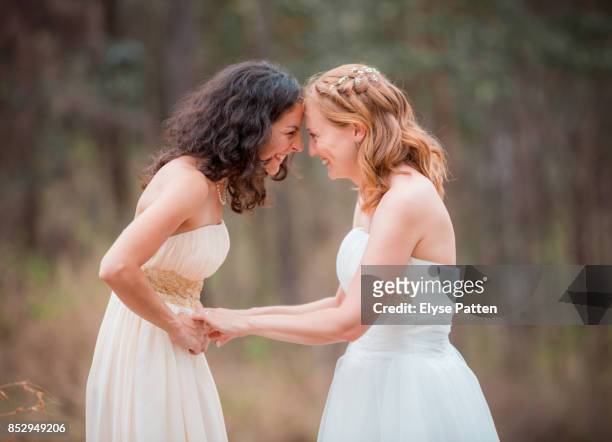 two brides share a moment of love and happiness following their wedding ceremony. an australian bush scene is in the background. - homohuwelijk stockfoto's en -beelden