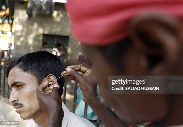 An Indian ear-cleaner tends to a customer on a street in Mumbai on March 8, 2009. Ear-cleaners, or Kaan Saaf Wallahs as they are locally known, in...