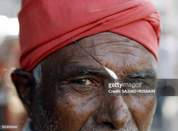 An Indian ear-cleaner wears a cotton swab in his trademark red turban is he waits for customers on a street in Mumbai on March 8, 2009. Ear-cleaners,...
