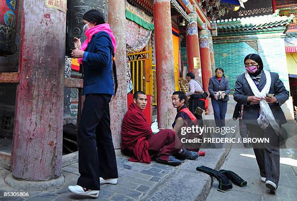 Tibetan Buddhist monks sit on the ground for a chat as pilgrims spin prayer wheels at the Kumbum Monastery outside of Xining on March 8, 2009 in...