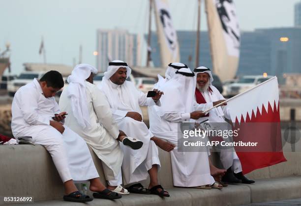 Qataris sit waving national flag as they gather in the streets to welcome back the Emir upon his returned from his first trip abroad during the...