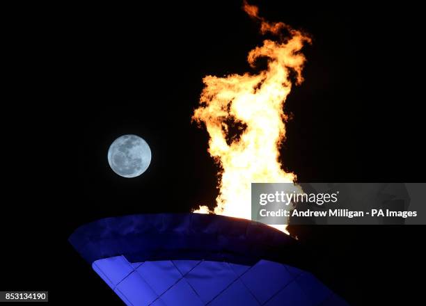 The moon is seen behind the Olympic flame at the 2014 Sochi Olympic Games in Sochi, Russia.