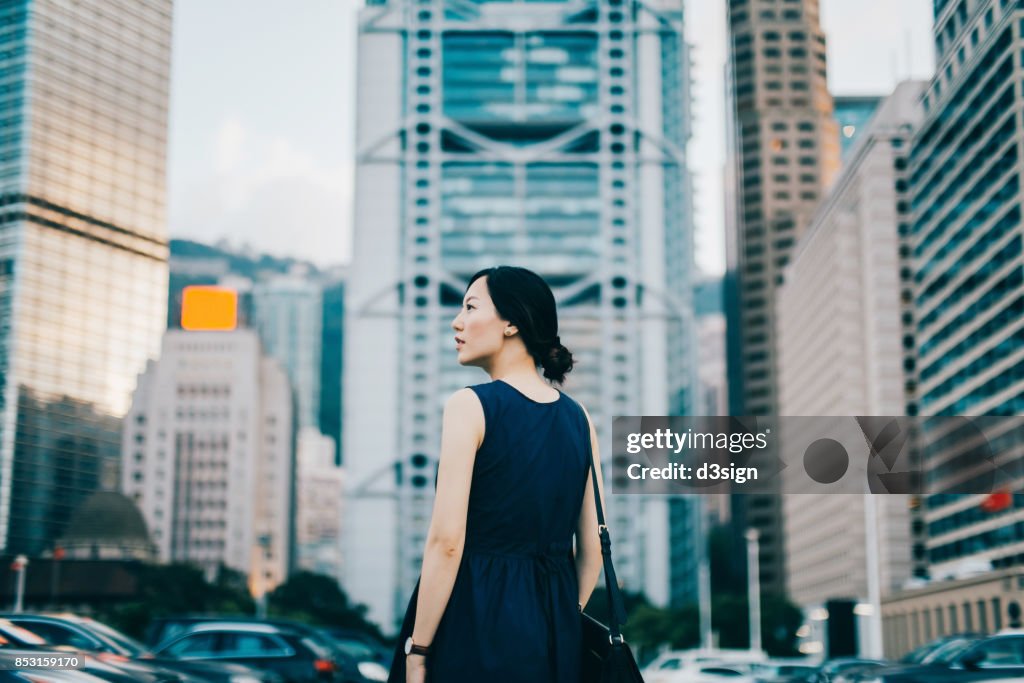 Successful young businesswoman looking away with confidence standing against urban cityscape