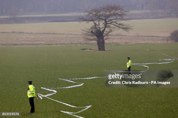 Police stand in a field along the cordon line close to the A146 after four people have died when a helicopter came down in thick fog in a field in...