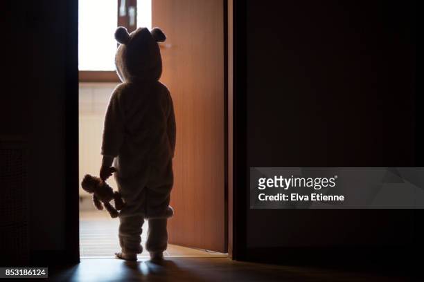 child in bear costume, standing in a darkened doorway, looking through to the light - one girl stock-fotos und bilder