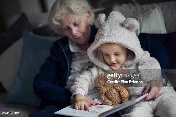 grandmother reading a story to a child wearig cozy bear onesie. - bear suit stock-fotos und bilder