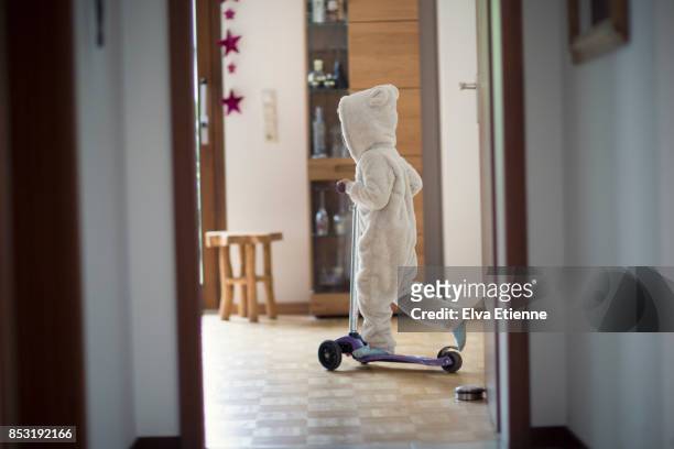 child (4-5) riding a push scooter in a house - bear suit stock-fotos und bilder
