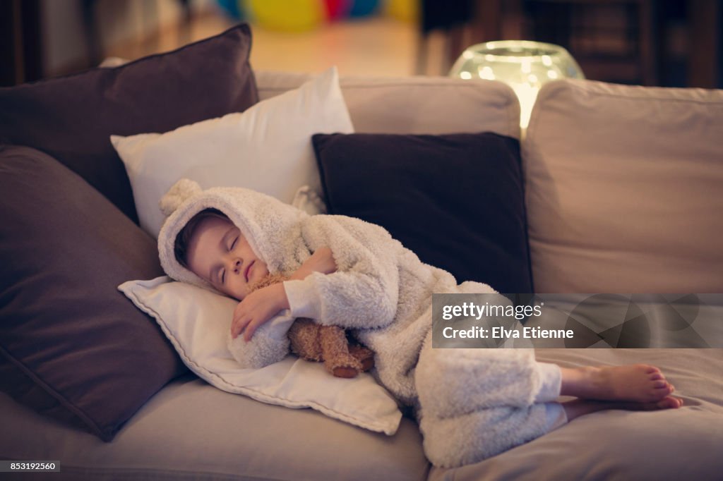 Tired child asleep on a sofa with teddy bear