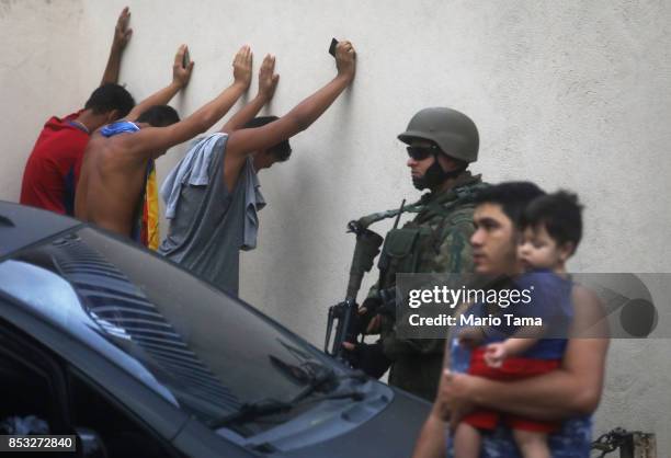 Brazilian soldier keeps watch as young men wait to be searched in the Rocinha 'favela' community on September 24, 2017 in Rio de Janeiro, Brazil. The...