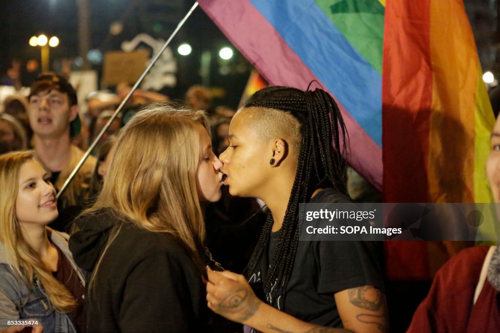 Two female protesters kiss under a rainbow flag. Hundreds of...