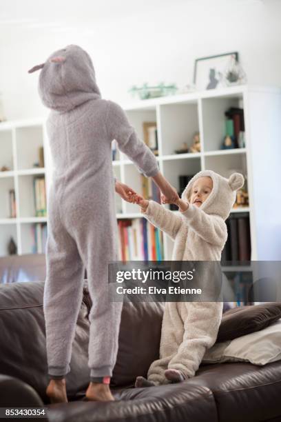 two girls in cozy hooded pyjamas, jumping on a sofa - bear suit 個照片及圖片檔
