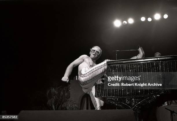 Photo of Elton JOHN; Elton John performing on stage, leg on piano