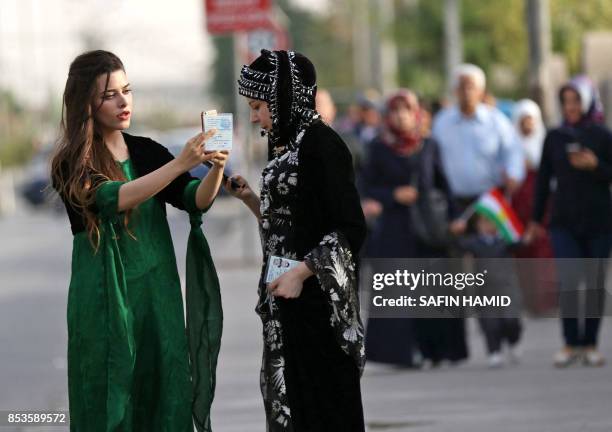 Iraqi Kurdish women uses their cell-phones as they hold on to their IDs while arriving to cast their votes in the referendum on independence at a...