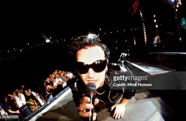 Photo of BONO and U2, Bono performing live onstage on Zoo TV Zooropa tour, wearing sunglasses, looking into camera, showing front rows of audience