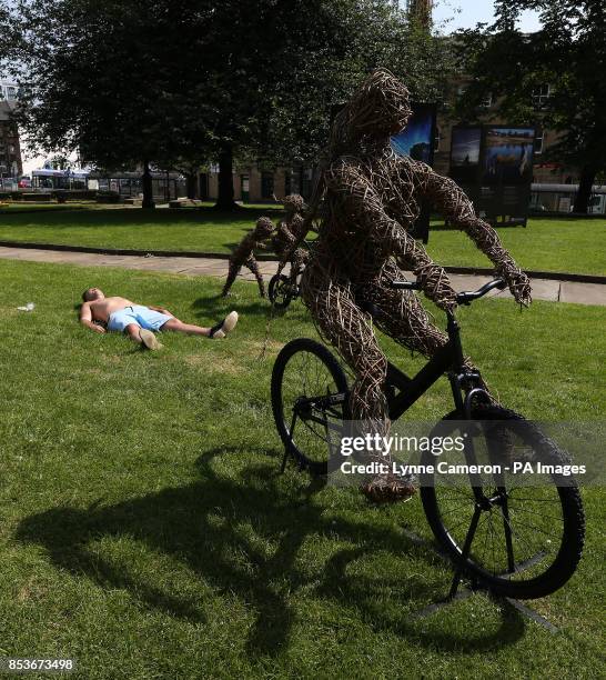 Man sunbathes next to 'La Grande Famille' a life-sized family of cyclists made of willow on steel armatures by the artist Carole Beavis in...