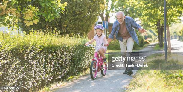 little girl learning ride a bike with grandfather - grandfather stock pictures, royalty-free photos & images