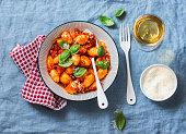 Potato gnocchi in tomato sauce with basil and parmesan and a glass of white wine on blue background, top view. Italian cuisine. Vegetarian food
