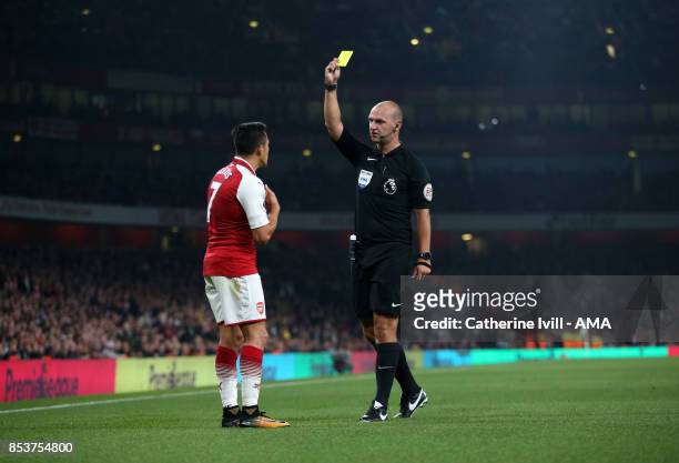 Referee Bobby Madley shows a yellow card to Alexis Sanchez of Arsenal during the Premier League match between Arsenal and West Bromwich Albion at...