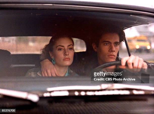 American actor Dana Ashbrook steers a car from behind the steering wheel with his other arm around the shoulders of actress Madchen Amick in a scene...