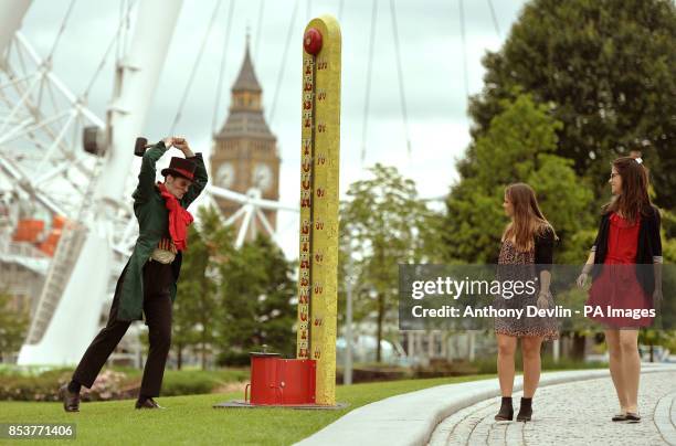 Stephanie Francis and Tansy Ratcliffe-James look-on as man in costume tests his strength on the High Striker during a photo call for the London...