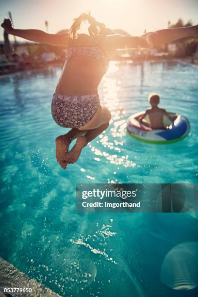 brother and sister playing in the resort pool - young girl jumping into swimming pool stock pictures, royalty-free photos & images