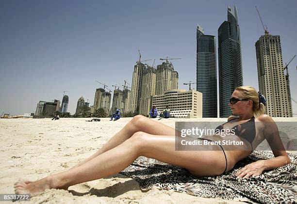 Migrant labourers stare at a sunbathing tourist as they take a break on a beach adjacent to the massive construction site on May 1, 2006 in Dubai,...