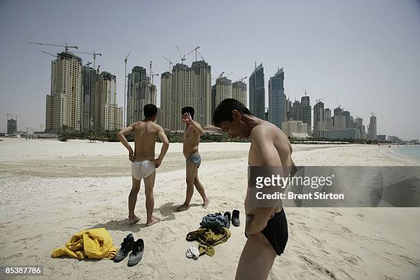 Nervous Asian migrant labourers avoid the camera as they take a swim on a tourist beach adjacent to the massive construction site which comprises...