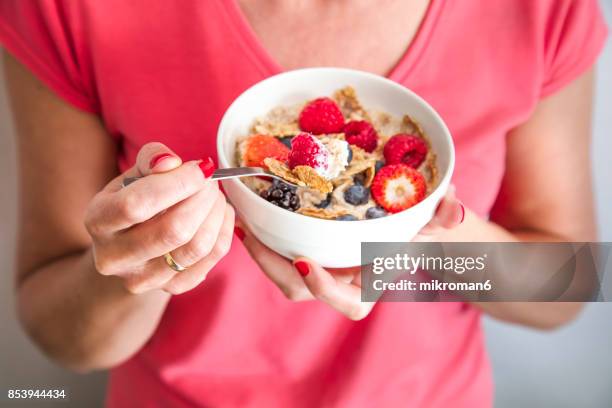 close-up crop of woman holding a bowl containing homemade granola or muesli with oat flakes, corn flakes, dried fruits with fresh berries. healthy breakfast - breakfast close stock pictures, royalty-free photos & images