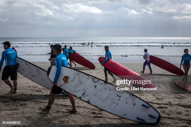 Tourists carry their surfboards at Kuta beach on September 26, 2017 in Kuta, Island of Bali, Indonesia. Indonesian authorities raised the alert level...