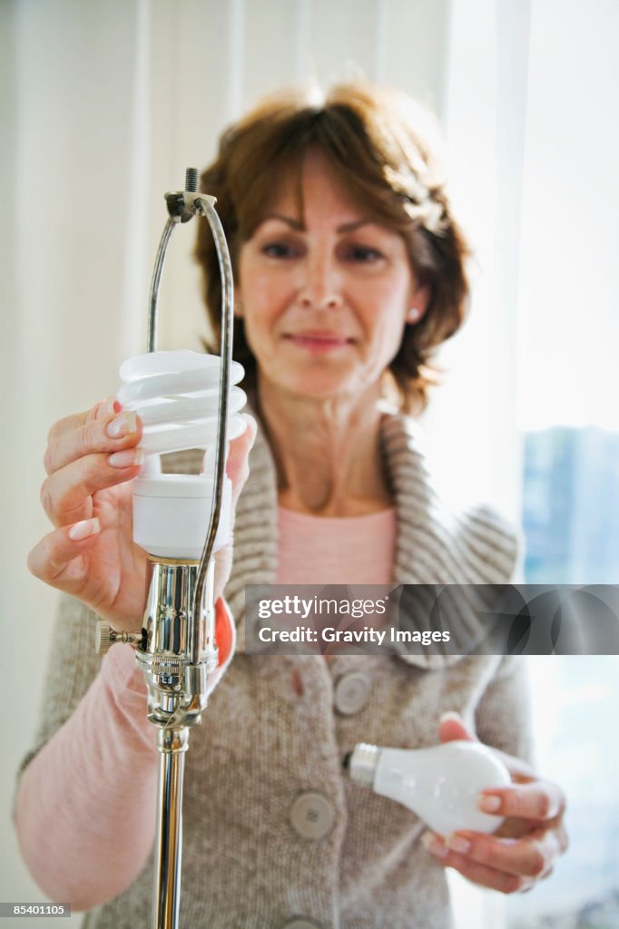 Mature women at home replacing light bulb