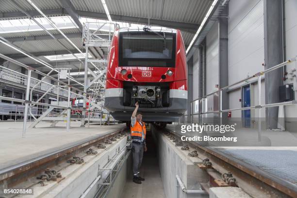 An employee stands beneath a Deutsche Bahn AG Alstom Coradia Lint railway train during final quality checks at the Alstom SA factory in Salzgitter,...