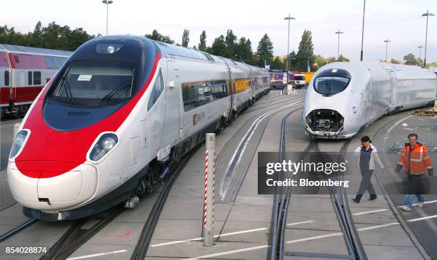 Workers walk past an Alstom SA Pendolino high-speed train, left, and a Siemens AG Velaro high-speed train as they sit on display prior to the opening...