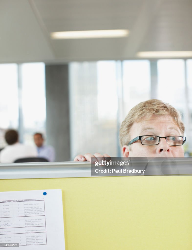 Businessman peering over cubicle wall