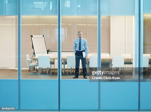 businessman standing at window in conference room - office solitude stock pictures, royalty-free photos & images