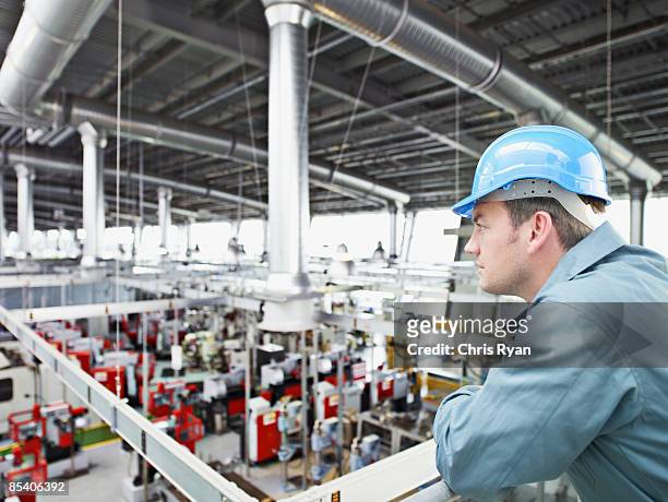 trabajador en una fábrica de difícil sombrero mirando a la planta de la fábrica - maquinaria de fábrica fotografías e imágenes de stock