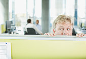 Businessman peering over cubicle wall