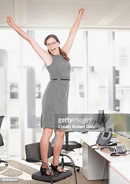 businesswoman at desk cheering - standing on chair stockfoto's en -beelden