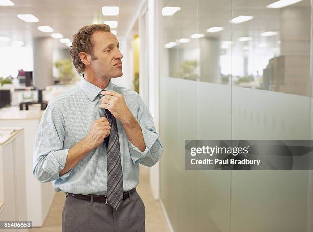 businessman adjusting tie in office - ijdel stockfoto's en -beelden