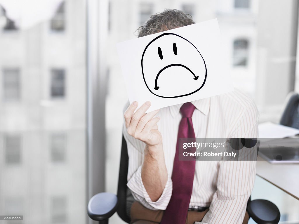 Businessman holding picture of sad face