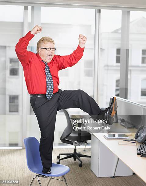 businessman at desk cheering - standing on chair stockfoto's en -beelden