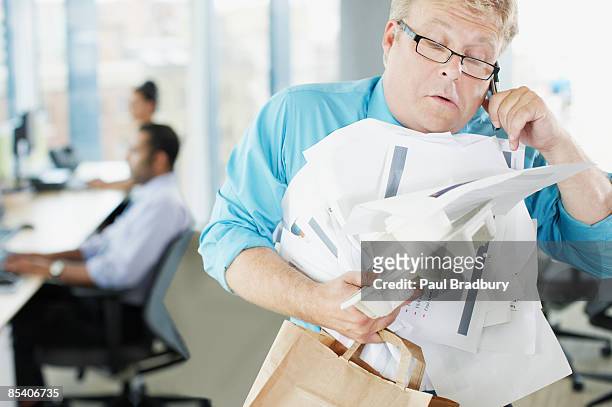 businessman talking on phone holding paperwork and coffee - work stress stockfoto's en -beelden