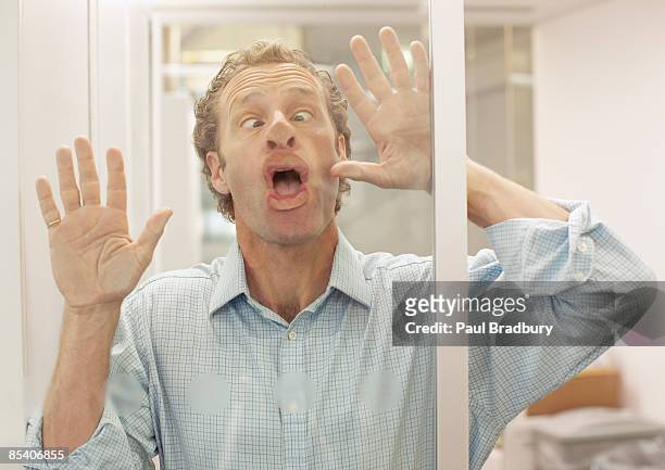 empresario haciendo frente a la pared de vidrio - poner caras fotografías e imágenes de stock