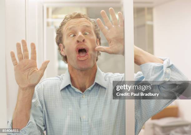 businessman making face on glass wall - scheel kijken stockfoto's en -beelden