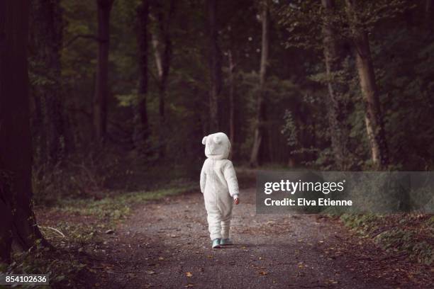 small child wearing white bear suit, walking along a tree-lined forest path - vulnerable children stock-fotos und bilder