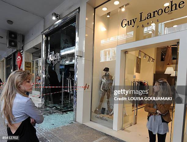 Shop attenders stand by a smashed exclusive shops in Athens central Kolonaki district, on March 13, 2009. A group of hooded youths armed with...