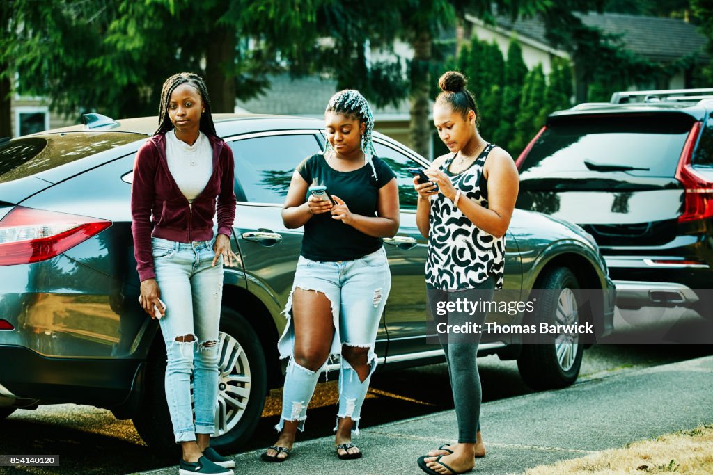 Teenage friends hanging out in front yard on summer evening looking at smartphones