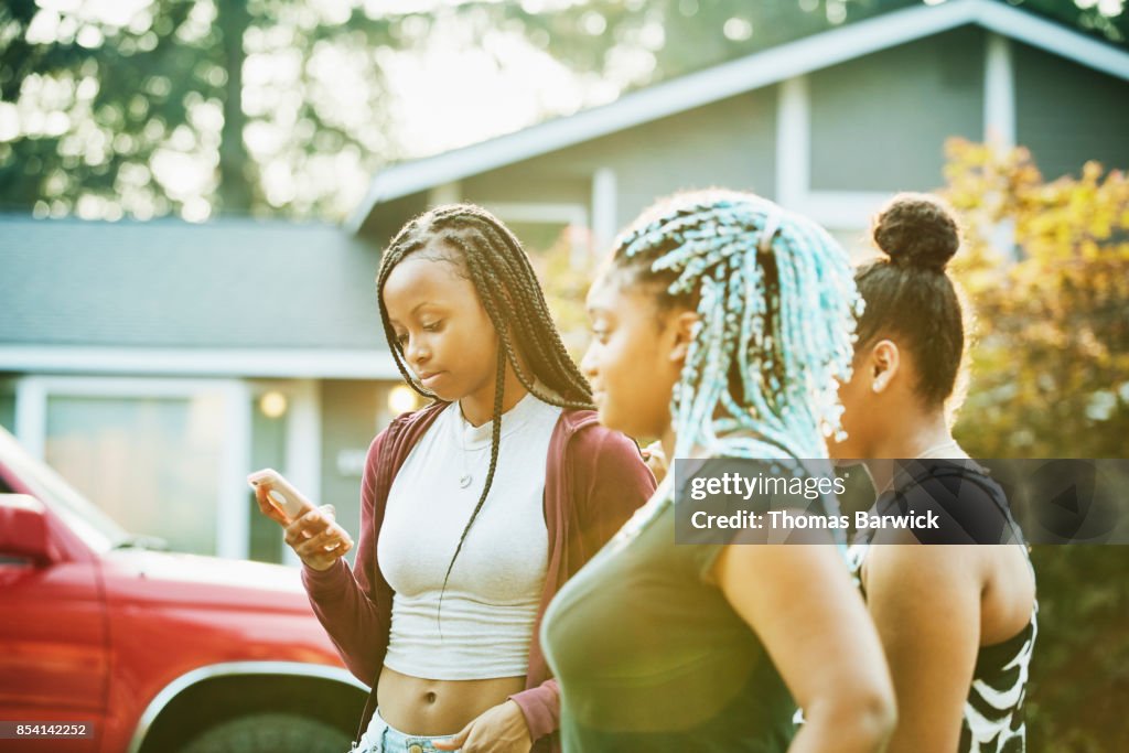 Young woman looking at smartphone while hanging out with friends on summer evening