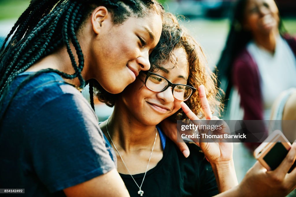 Smiling teenage friends taking selfie with smartphone on summer evening