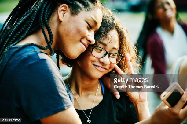 Smiling teenage friends taking selfie with smartphone on summer evening